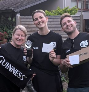 Die drei Sieger*innen der Vereinsmeisterschaft 2026: Sina (1. Platz, hält den Pokal), Jens (2. Platz, hält Jameson) und Monika (3. Platz, hält Guinness-Handtuch) lächeln in die Kamera. (Keyword: Vereinsmeisterin).